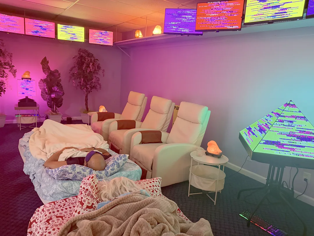 Two guests asleep on cots under soft blankets, the recliners and the glowing pyramid around them.