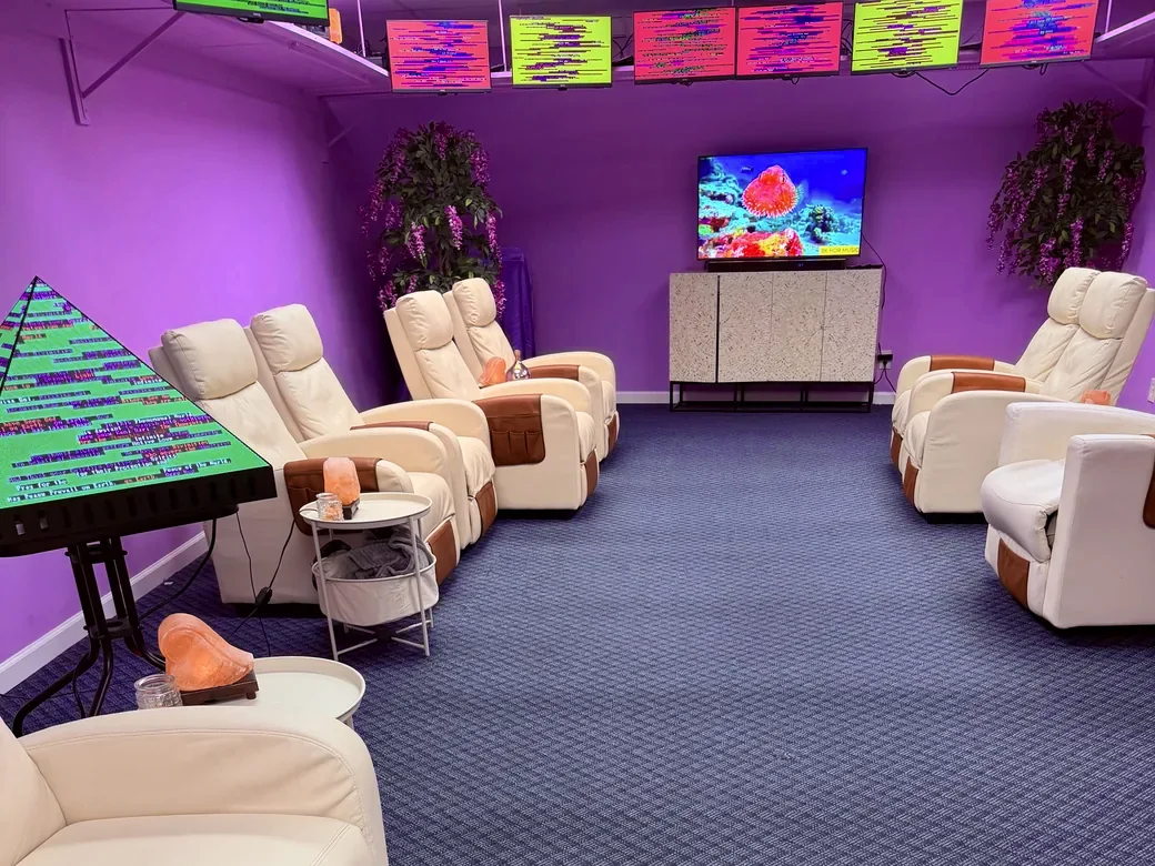 Rows of white recliners facing a large screen showing a nature scene, with plants and the pyramid in the corner.