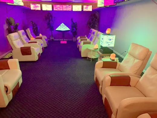 The room in blue light: two rows of recliners leading to the pyramid, screens glowing along the ceiling.