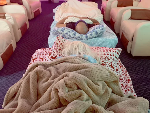 Two guests asleep on cots under soft blankets between the recliners during an overnight.