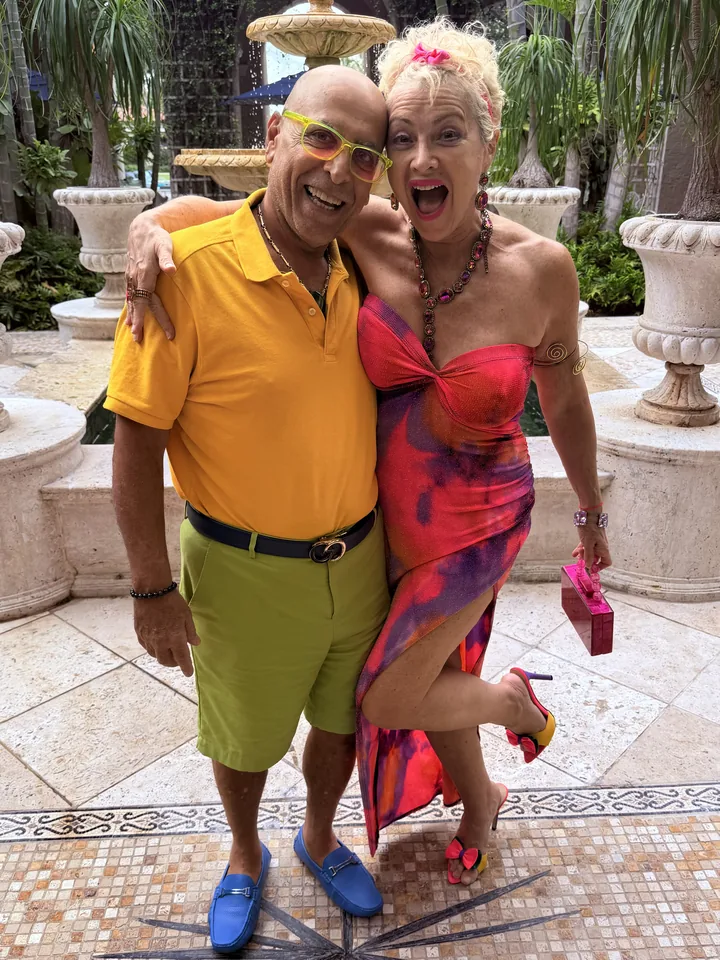 Frannie and Dani laughing arm in arm beside a courtyard fountain, Dani in a yellow shirt and green shorts, Frannie in a red and purple dress.